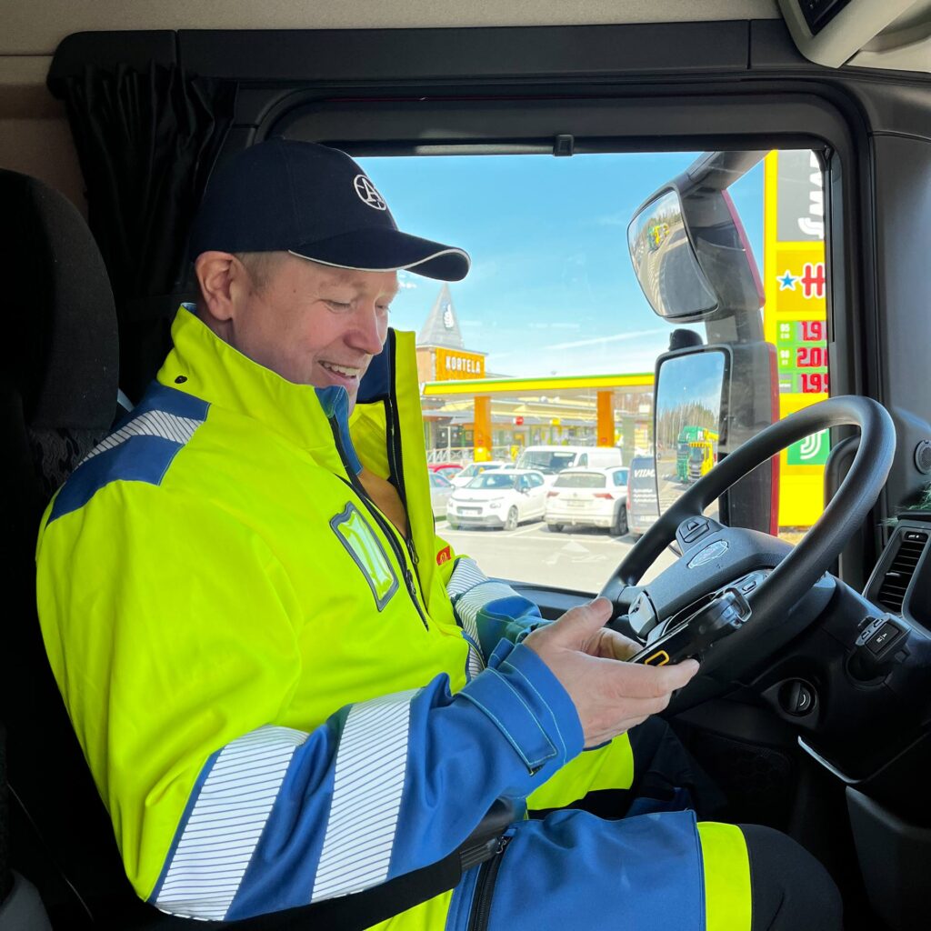 Jarmo Karonen istuu autossaan ja pitää kädessään mobiililaitetta.